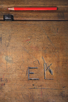 close up of wooden school desk with red pencil and carved initials