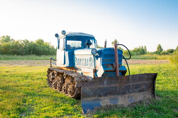 Fototapeta premium Rural farm field landscape. Soviet blue crawler bulldozer, front view