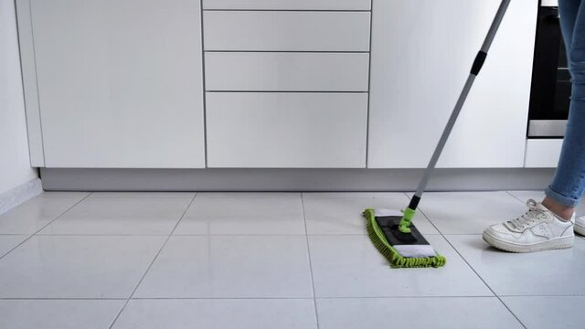 Woman washing white kitchen floor with special swob, cleaning service, close-up