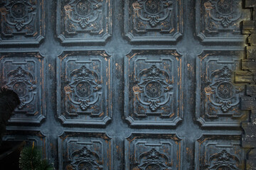 The texture of a rough plastered gray-black wall. The walls with raised decorative plaster and repeated bas-reliefs are painted with dark paint. Old vintage background.