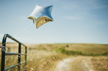Silver star balloon blowing on windy day near open grass field in California