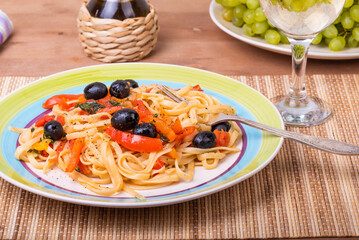 Classic Italian pasta with vegetables, linguine with sweet peppers, tomatoes and olives on a plate on a napkin on the table, close-up