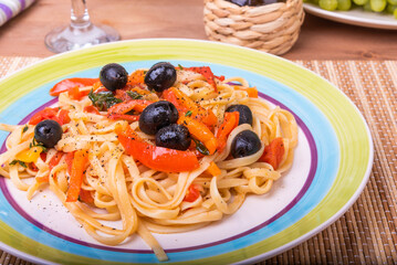 Classic Italian pasta with vegetables, linguine with sweet peppers, tomatoes and olives on a plate on a napkin on the table, close-up