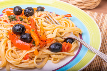 Classic Italian pasta with vegetables, linguine with sweet peppers, tomatoes and olives on a plate on a napkin on the table, close-up