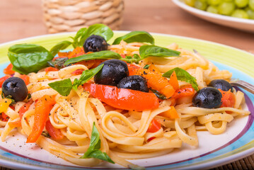 Classic Italian pasta with vegetables, linguine with sweet peppers, tomatoes and olives on a plate on a napkin on the table, close-up