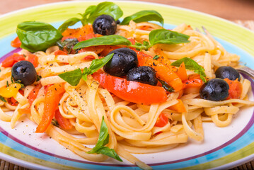 Classic Italian pasta with vegetables, linguine with sweet peppers, tomatoes and olives on a plate on a napkin on the table, close-up