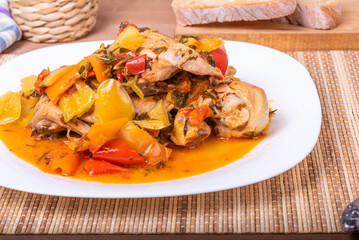 Italian chicken stew - chicken with bell peppers in a plate on a napkin with cutlery - classic Italian recipe, close-up, top view