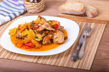 Italian chicken stew - chicken with bell peppers in a plate on a napkin with cutlery - classic Italian recipe, close-up, top view