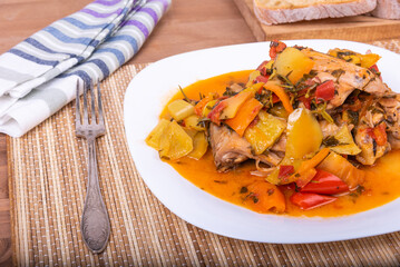 Chicken with bell peppers in a plate on a napkin with cutlery - classic Italian recipe, close-up, top view