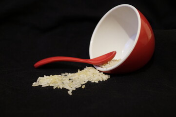 A toppled red dish with rice and a spoon
