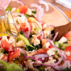 Cooking Italian Tuscan panzanella salad - olive oil is poured into a salad of bread, cucumbers, tomatoes, red onions, olive oil in a glass bowl