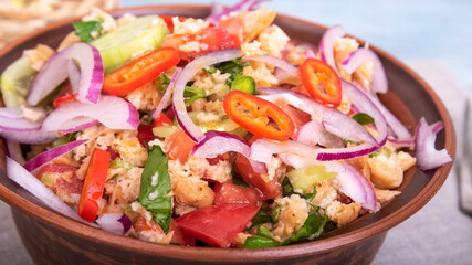 Italian tuscan vegetarian panzanella salad, mixed bread, tomato and vegetable salad in a clay bowl on a linen napkin on a rustic blue wooden table