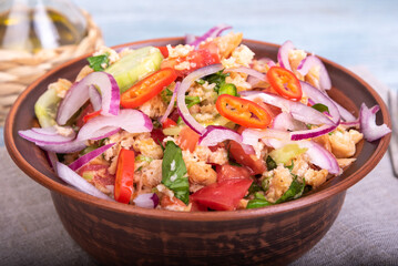 Italian tuscan vegetarian panzanella salad, mixed bread, tomato and vegetable salad in a clay bowl on a linen napkin on a rustic blue wooden table