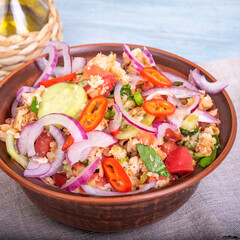 Italian tuscan vegetarian panzanella salad, mixed bread, tomato and vegetable salad in a clay bowl on a linen napkin on a rustic blue wooden table
