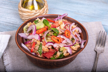 Italian tuscan vegetarian panzanella salad, mixed bread, tomato and vegetable salad in a clay bowl on a linen napkin on a rustic blue wooden table