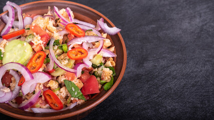 Italian tuscan vegetarian panzanella salad, mixed salad of breads, tomatoes and vegetables in a clay bowl on a black stone surface, top view, copy space