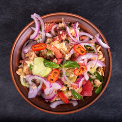 Italian tuscan vegetarian panzanella salad, mixed salad of bread, tomato and vegetables in a clay bowl on a black stone surface, top view, close-up