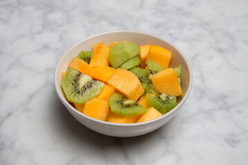 Fruit bowl with kiwi and peach on a marble table