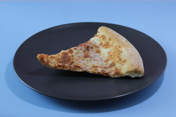 Dried slice of pizza on a black table on a blue background. Food concept.