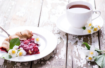 Cup of black fragrant tea and tasty piece of homemade strawberry cake on a on a wooden background jasmine branch. Place for text.