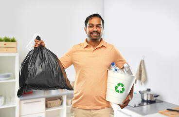 recycling, sorting and sustainability concept - smiling young indian man holding bucket with...