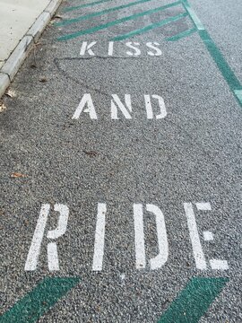 Painted message on the road in a school zone that reads ""KISS AND RIDE""