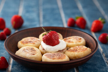 Food poster - Cottage cheese pancakes, pancakes, cheesecakes with strawberries in a clay plate on a background of blue wooden boards. Ukrainian and Russian cuisine. Homemade food. Tasty breakfast.