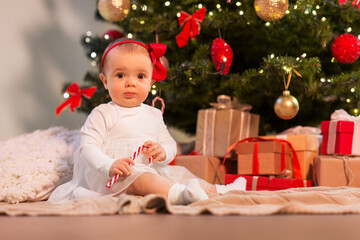 Obraz na płótnie Canvas holidays and childhood concept - sweet baby girl at christmas tree with gifts at home