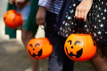 Close-up of children with pumpkins bags playing trick or treat outdoors - obrazy, fototapety, plakaty