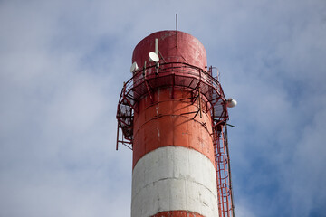 Close up of a smokeless chimney smokestack in red and white stripes on a sunny day against the blu sky