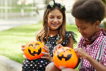 Happy children sitting outdoors and looking at pumpkins bags full of sweets