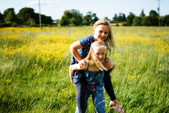 2 little girls giving each other piggy-backs outdoors