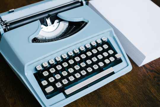 retro 60s blue typewriter with a ream of blank paper