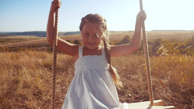 little girl kid swinging on a wooden swing on a tree in the park. happy family kid dream concept. little kid girl playing on fun wooden swing on tree fun dream concept in park