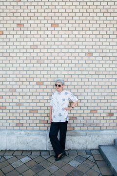 Senior woman leaning against a big brick wall