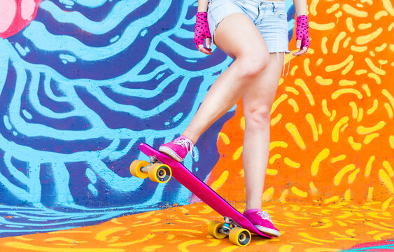 Hip skateboard girl driving her skate on funky colorful graffiti background .