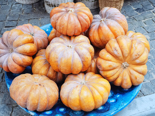 A blue ceramic bowl with orange pumpkins stands on rough paving slabs outside