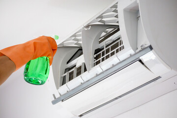 Asian man cleaning air conditioner with spray bottle