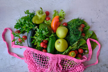 Fresh green and red vegetables and fruits in pink meshon on grey background. Top view. Healthy food, natural products. Concept-reusable bag.