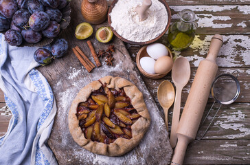 Homemade pie from plums with ingredients and fresh fruits on a wooden board.