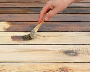 Hand holding a brush applying varnish paint on a wooden surface. Board half painted. Applying a protective varnish to a wooden board, table or floor.