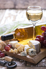 White wine glass with full bottle and cheese on a wooden board.