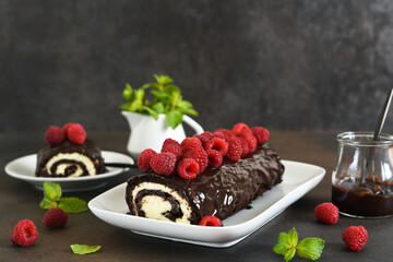 Chocolate roll with cream cheese and raspberries, with a cup of coffee on a dark background.