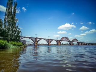 View of the Merefa-Kherson bridge across the Dnieper river in Dnipro (Ukraine). Beautiful landscape with an old concrete structure with arches and pillars on the background of the water surface