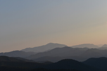 Weite Landschaft mit zum Horizont hin verschwimmenden Bergen und Hügeln in Abendstimmung, warme Farben
