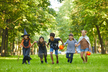 Group of children in Halloween costumes running on green grass in the park they having fun at the party