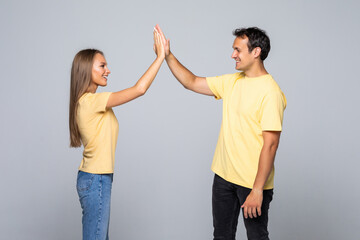 Portrait of a beautiful young couple standing and giving high five on the gray background