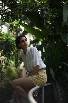 Young stylish woman sitting on the fence in the botanical garden