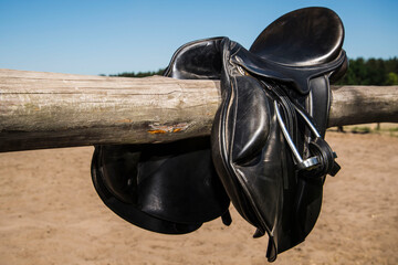 Black leather horse saddle on a wooden horizontal fence.