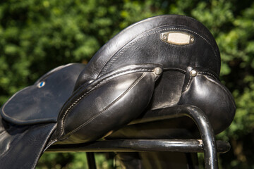 Back view of leather horse saddle on a blurred natural background.